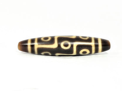 At-071126-9E8 face A, nine eye dzi 57.6×12.7mm, dark brown, sharp tapered end, warm cream motif lines, unretouched