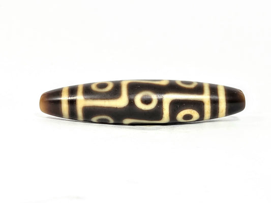 At-071126-9E8 face A, nine eye dzi 57.6×12.7mm, dark brown, sharp tapered end, warm cream motif lines, unretouched