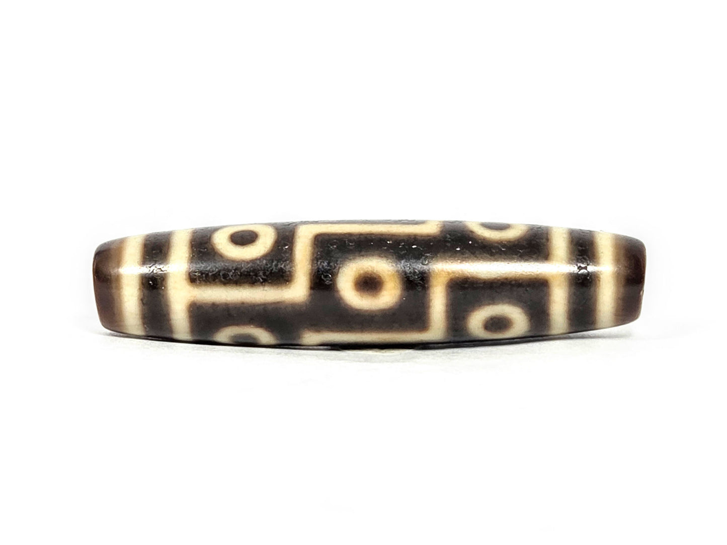 At-071126-9E6 face A, antique nine eye Tibetan dzi 54.8×12.6mm, very dark brown ground, cream motif lines, 300–500 yrs, unretouched