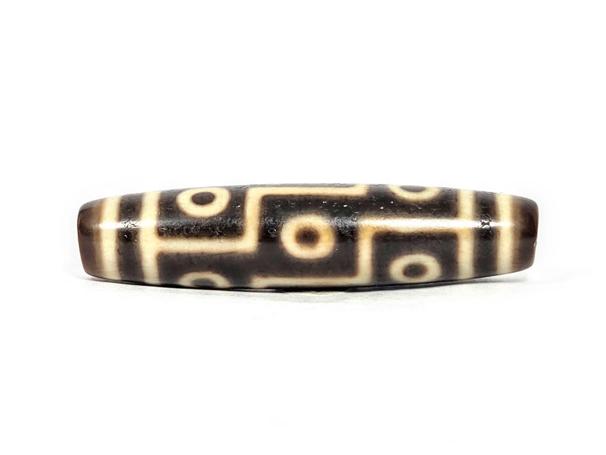 At-071126-9E6 face A, antique nine eye Tibetan dzi 54.8×12.6mm, very dark brown ground, cream motif lines, 300–500 yrs, unretouched