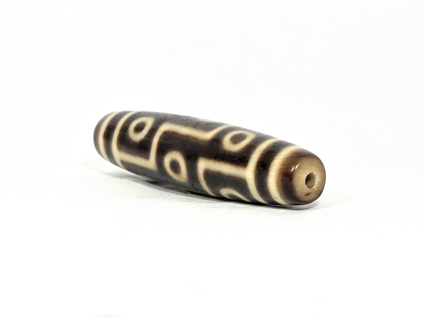 At-071126-9E6 drill-hole end cap, warm cream-beige, small clean centred hole, motif lines visible on body, unretouched