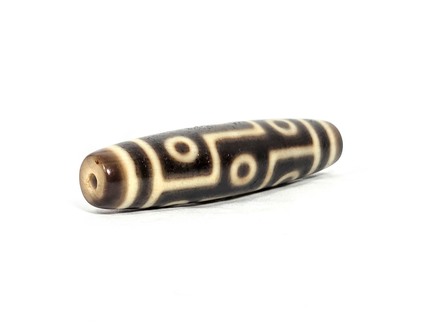 At-071126-9E6 opposite drill-hole end, warm cream-beige end cap, small clean hole, nine eye motif to end boundary, unretouched