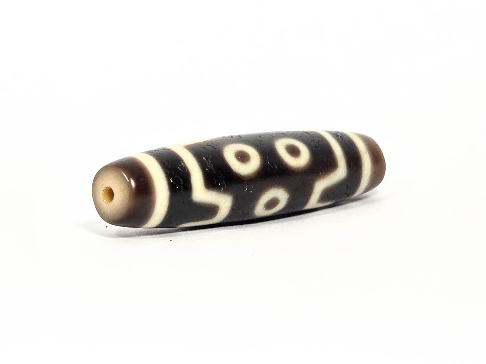 At-072226-7E end angle B — opposite cream-beige end cap, pitch-black body, seven eye motif wrapping, unretouched