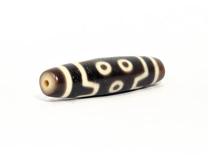 At-072226-7E end angle B — opposite cream-beige end cap, pitch-black body, seven eye motif wrapping, unretouched