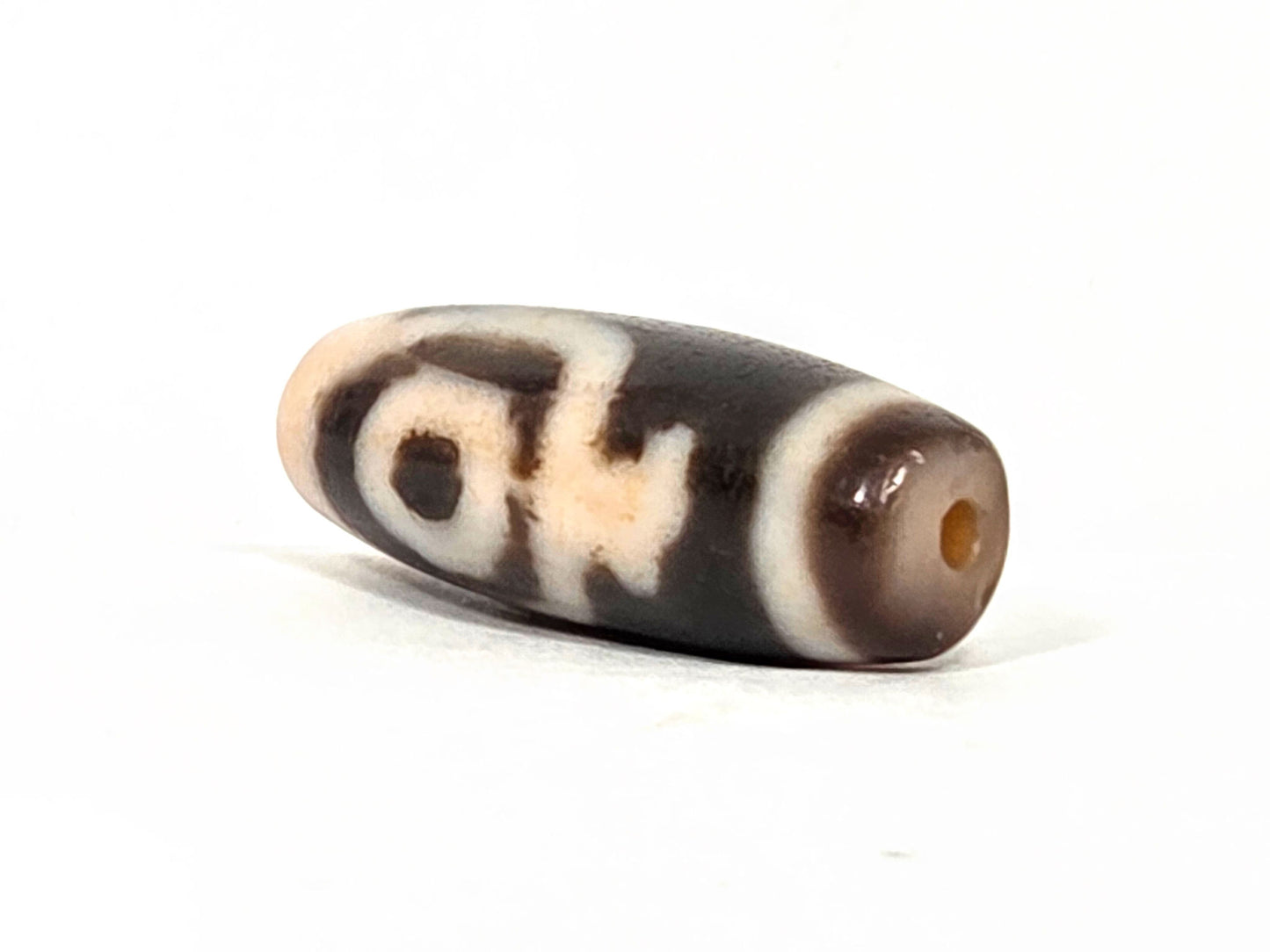 At-062226-2ETV2, end view showing peachy-cream end cap, drill hole intact, dark brown body, fusiform taper, unretouched