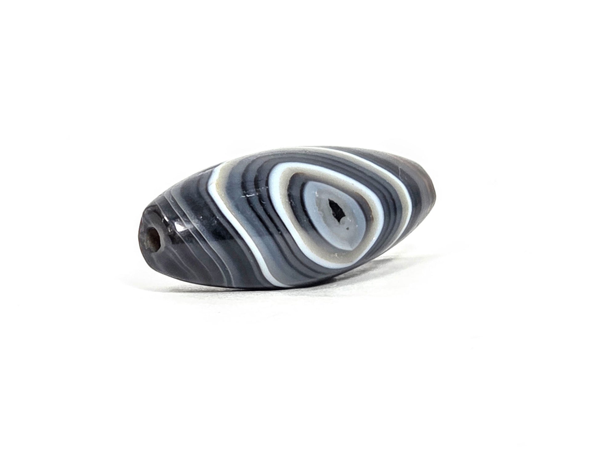N-N-071026-1E-OLV2 drill hole end view, tapered olive point, eye motif on curved face, dark grey-brown banding, unretouched