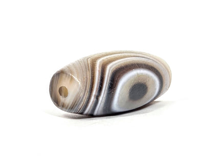 N-N-062126-1E2 dzi bead, angled view showing drill hole at narrow end, unretouched