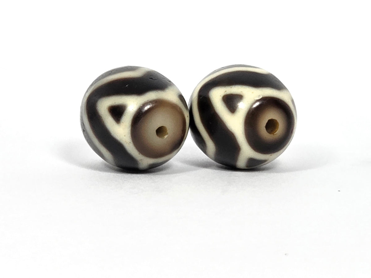 At-070626-TTW antique round Wave Tiger Tooth dzi pair, opposite drill-end view: Bead A cream-grey end, Bead B warm honey-brown end, motif elements visible, unretouched