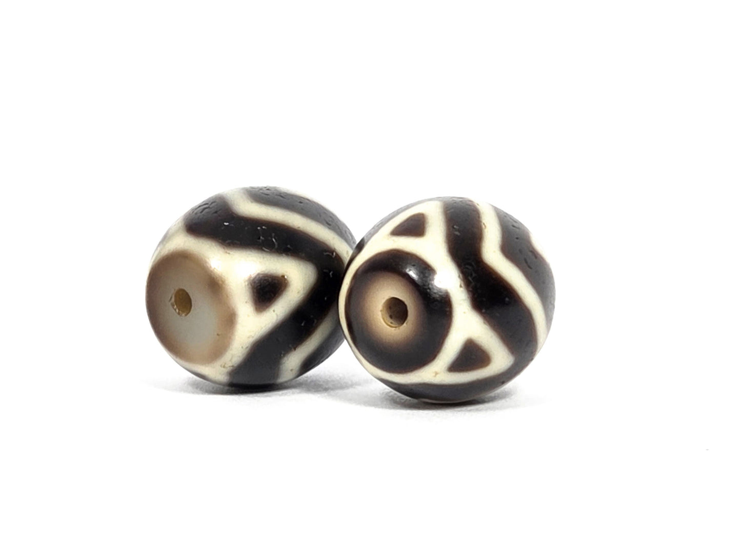 At-070626-TTW antique round Wave Tiger Tooth dzi pair, opposite drill-end view: Bead A cream-grey end, Bead B warm honey-brown end, motif elements visible, unretouched