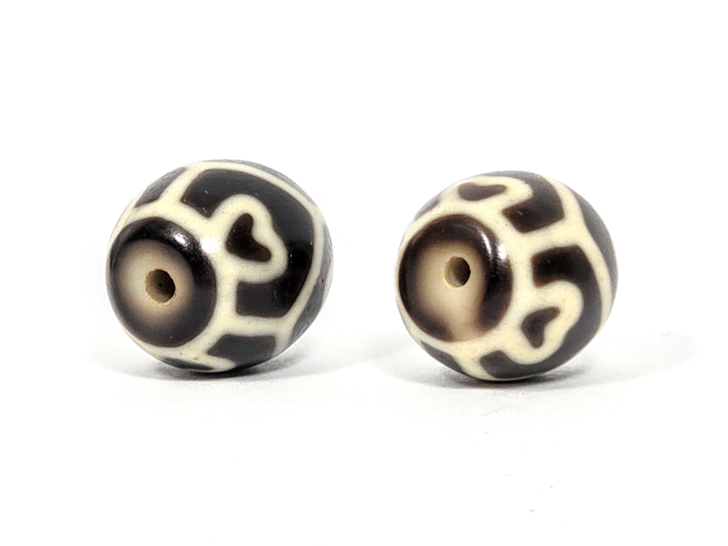 Drill hole end view of antique Tibetan Six Eye Lotus round Dzi bead pair showing swirl and lotus petal pattern surrounding natural agate drill holes — unretouched photo — Ancient Dzi Shop