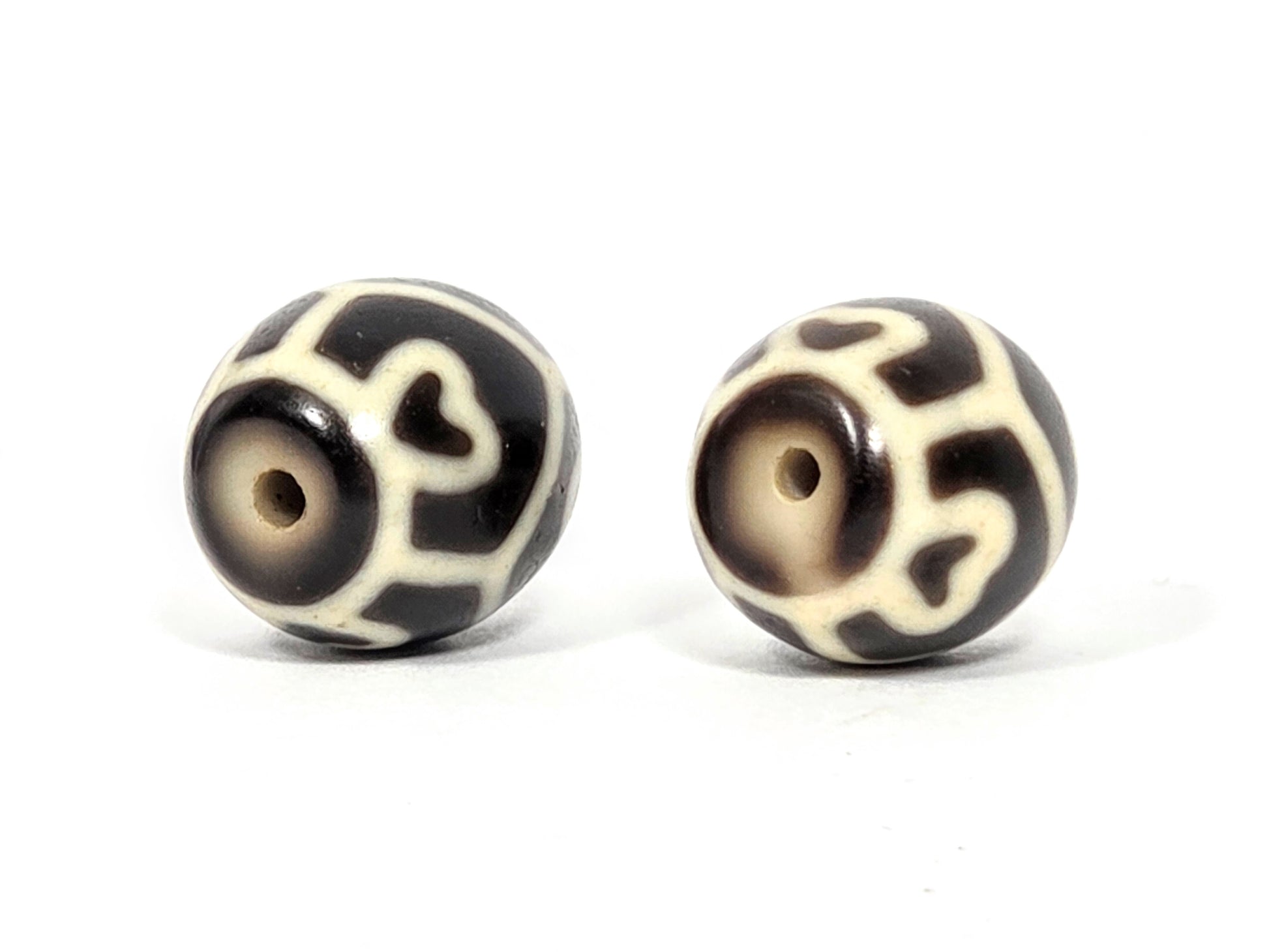 Drill hole end view of antique Tibetan Six Eye Lotus round Dzi bead pair showing swirl and lotus petal pattern surrounding natural agate drill holes — unretouched photo — Ancient Dzi Shop