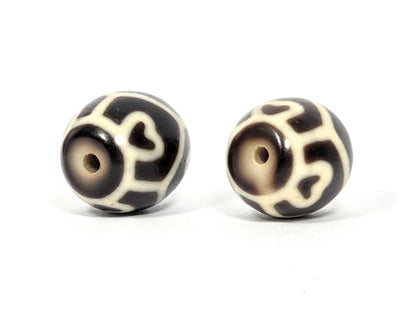 Drill hole end view of antique Tibetan Six Eye Lotus round Dzi bead pair showing swirl and lotus petal pattern surrounding natural agate drill holes — unretouched photo — Ancient Dzi Shop