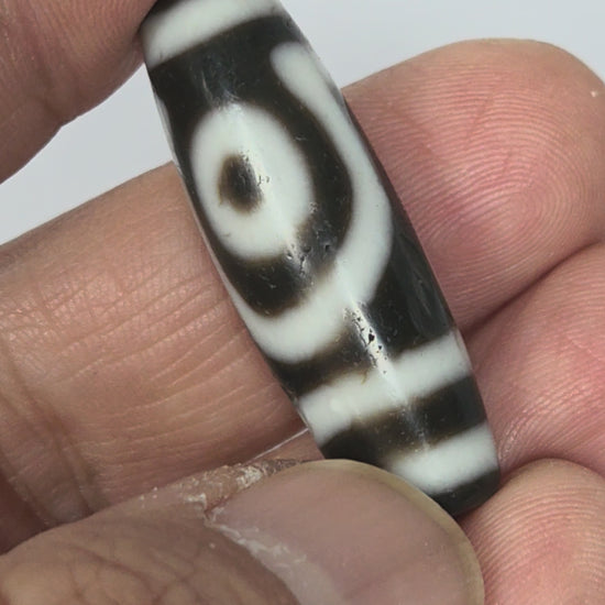 Video of antique Tibetan two eye dzi bead At-010726-2E3 rotating 360°, both closed concentric-ring eyes visible, medicine digs, near-black natural agate, 38.6mm × 12.5mm, unretouched footage