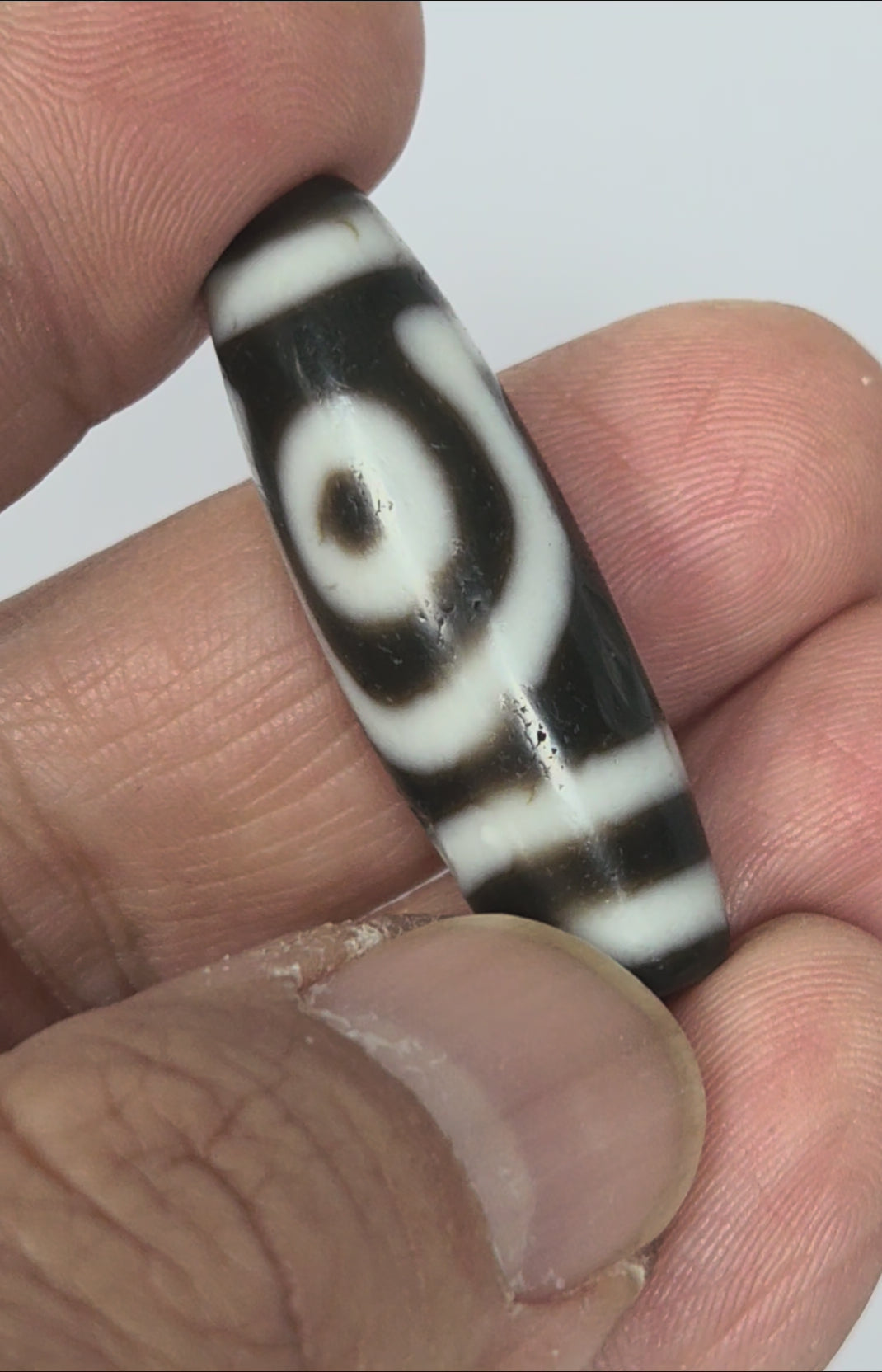 Video of antique Tibetan two eye dzi bead At-010726-2E3 rotating 360°, both closed concentric-ring eyes visible, medicine digs, near-black natural agate, 38.6mm × 12.5mm, unretouched footage