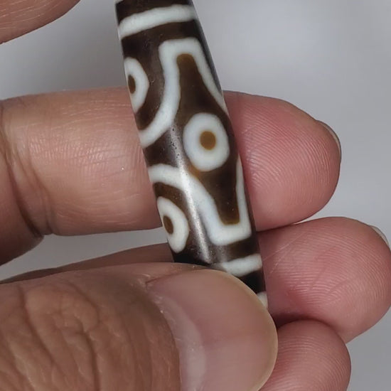 Video of antique Tibetan six eye dzi At-053026-6E rotating 360°, four faces — diamond frame, open-ring pair, closed-ring pair, honey-gold end caps, deep brown agate, 54.9mm, unretouched footage
