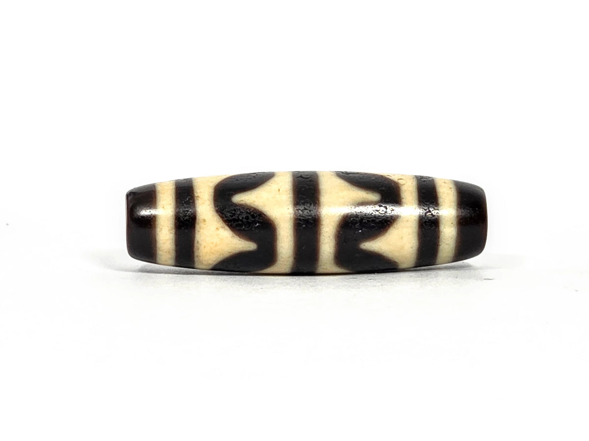 Third lateral profile of antique double wave dzi bead (AT-092826-DW) showing full motif composition, deep black wave forms on cream-white ground, 41.1 mm × 11.7 mm