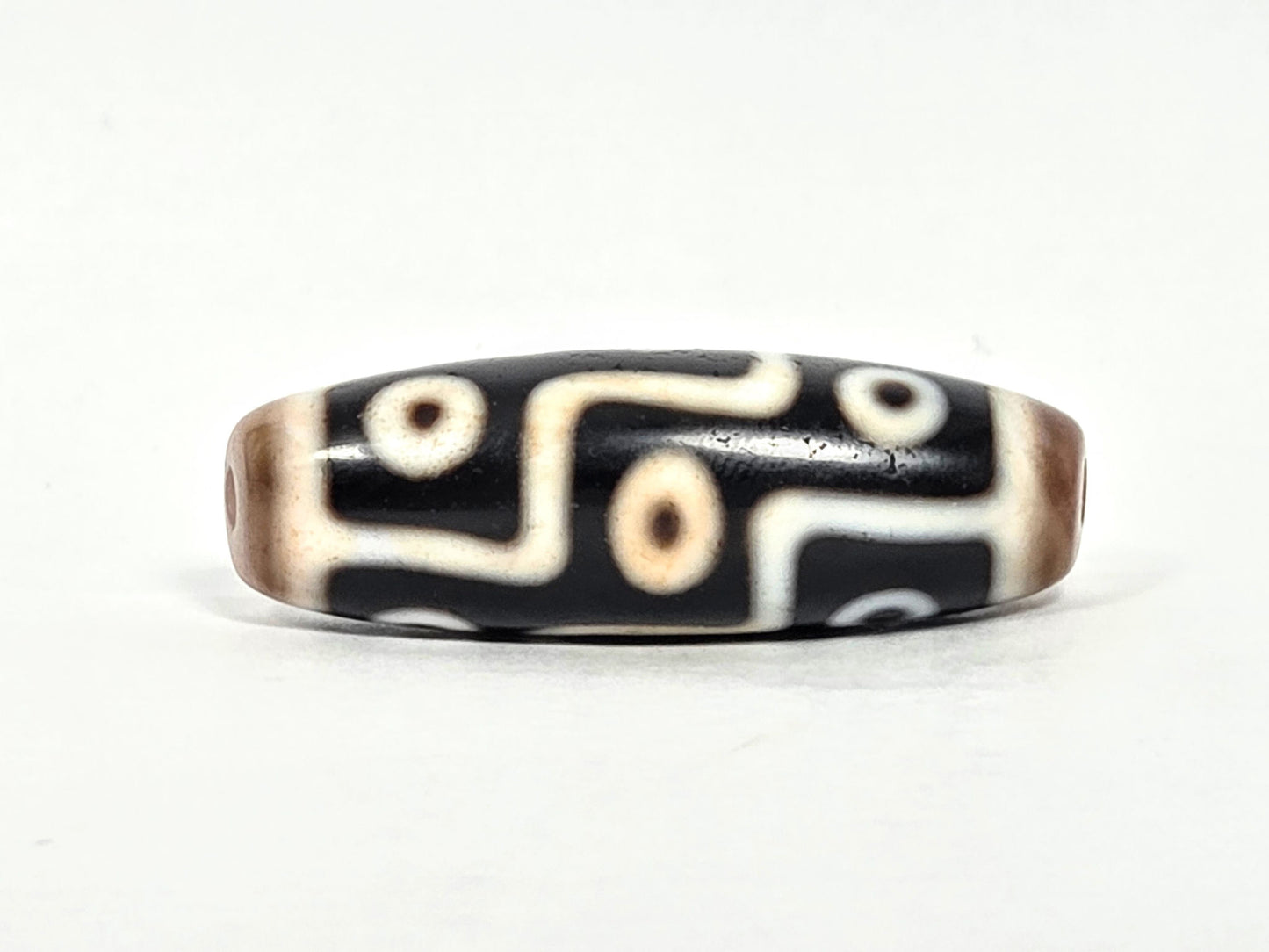At-070626-9E2 nine eye dzi face B, pitch-black ground, warm brown end caps, cream stepped motif rotated, unretouched