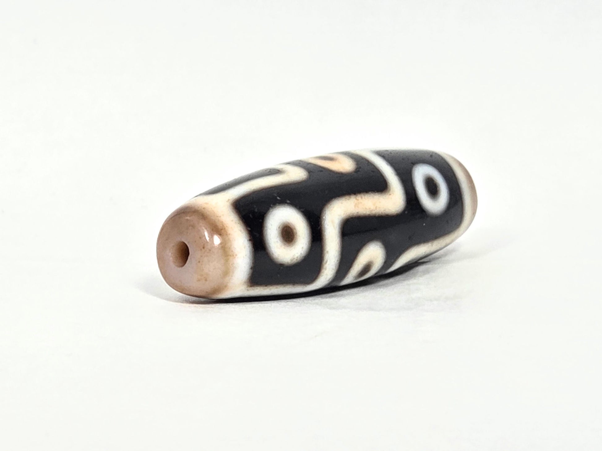 At-070626-9E2 nine eye dzi, drill end B, warm brown domed cap, cream eye motif, pitch-black body, unretouched