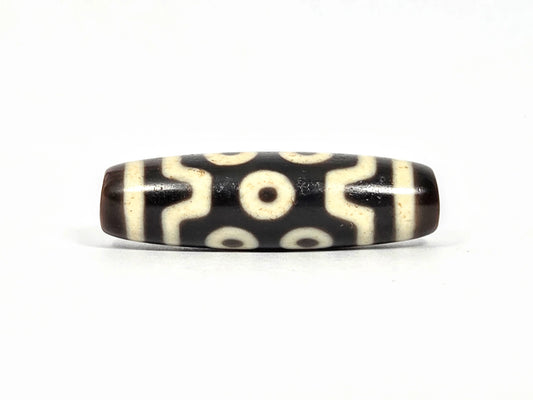 Antique Tibetan seven-eye dzi bead (AT-092826-7E), first lateral profile showing three eyes in upper and lower registers with S-curve wave connectors on deep dark brown-black agate, 39.7 mm, 200–400 years old