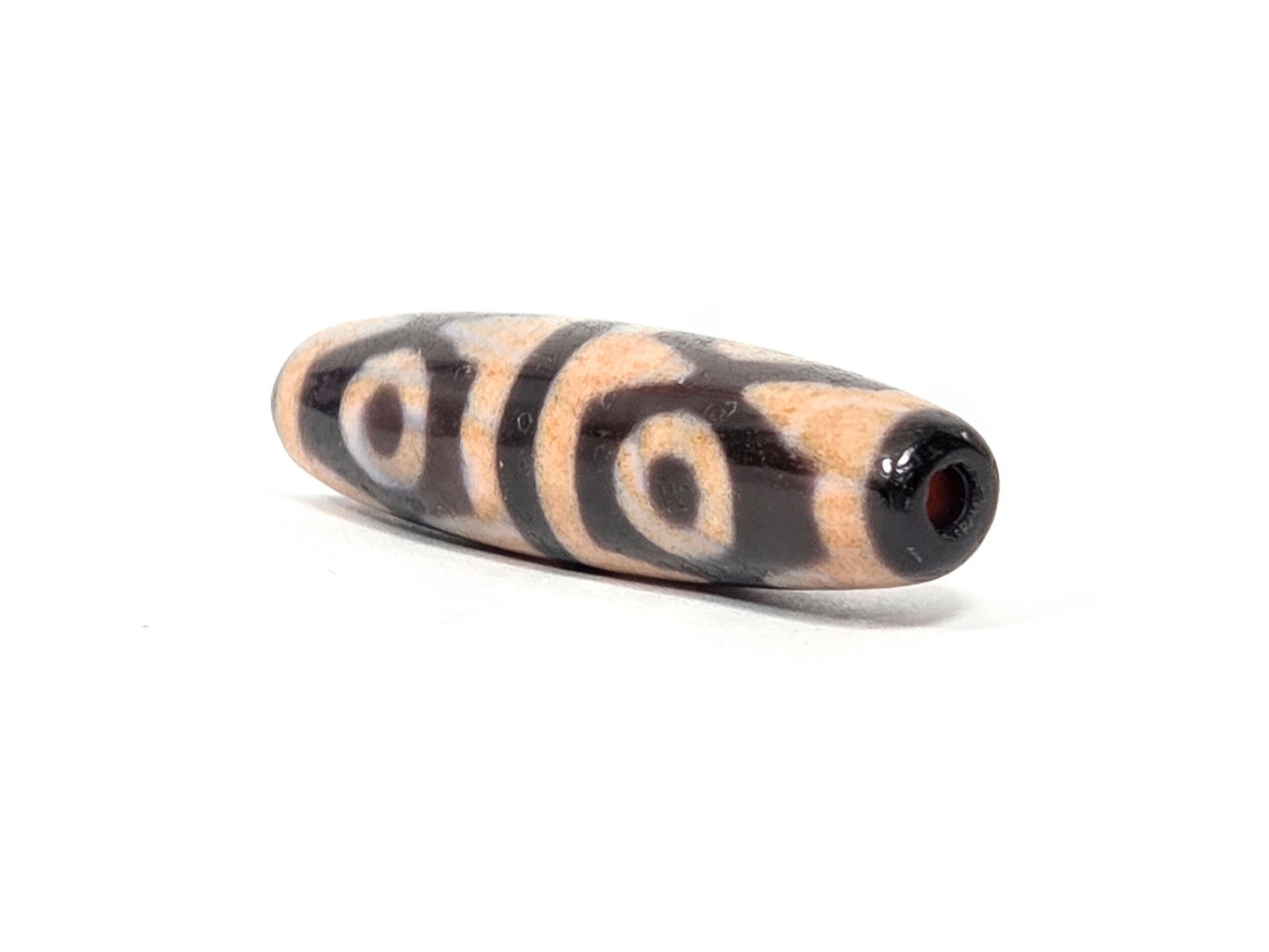 V-061026-6ETTBS angled end, drill hole with warm reddish interior, dark end cap, eye rings wrapping body, unretouched